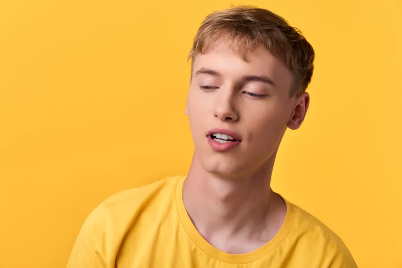 Young man in a bright yellow shirt stands before a vivid yellow background, eyes closed and face relaxed, creating a calm mood with a clean studio look, soft light and smooth skin under controlled