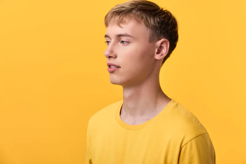Man in yellow shirt against solid yellow background, closeup and solo, calm expression with model gaze, studio lighting and minimal setup for fashion, lifestyle or branding use