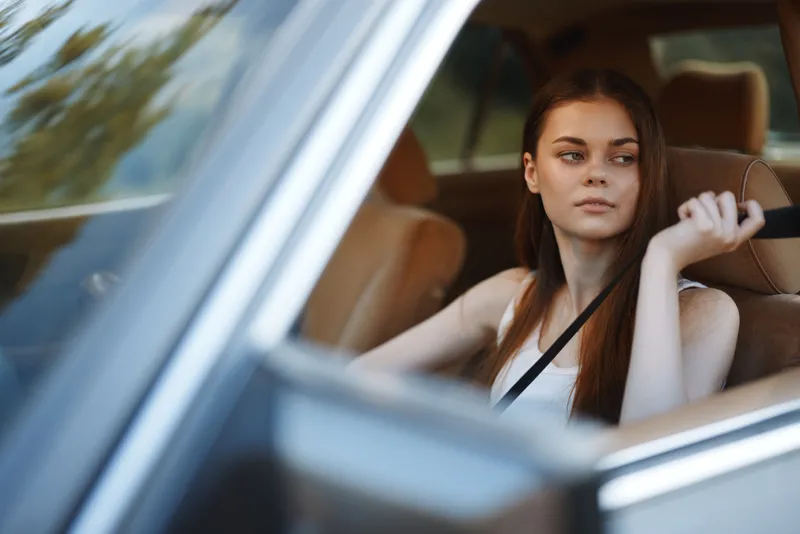 Young woman sitting in a car with a thoughtful expression, highlighting modern lifestyle and freedom.