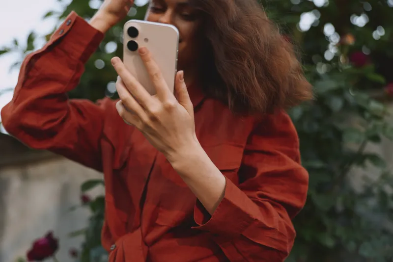 Woman lifestyle, selfie outdoors in a red coat, smiling while filming on a phone, casual urban setting, natural light, candid portrait