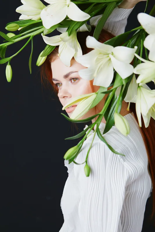 Elegant woman in a white shirt adorned with fresh lilies on a dark background, portraying beauty and grace in a floral themed composition