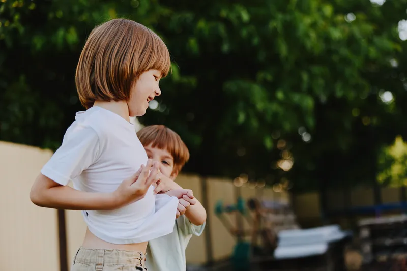 Two playful boys enjoying a sunny day outdoors, laughing together and engaging in friendly playfulness, surrounded by greenery and warm sunlight.