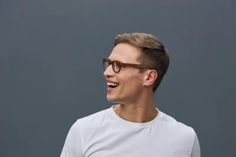 Smiling man with glasses and short brown hair wearing white t-shirt, looking to the right, isolated on gray background. Casual, happy, cheerful expression. People lifestyle concept.