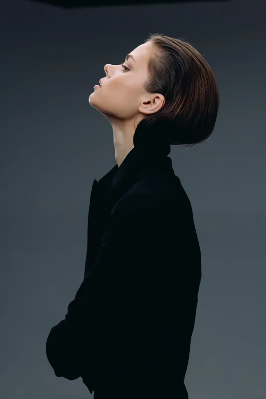 Profile of thoughtful woman posing with eyes closed in dark outfit on grey background
