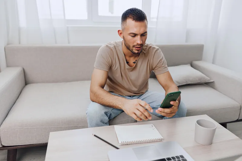 Focused man using smartphone while sitting on a cozy couch, showcasing modern lifestyle. Perfect for themes of productivity and technology.