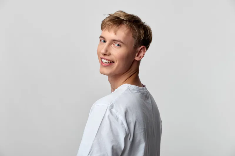 Smile, man in casual white shirt in a studio with gray background, exuding happy youth and confident ease, ideal for lifestyle and fashion projects seeking approachable energy
