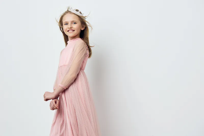 Smiling girl in a pink dress with flowing fabric, showcasing joy and elegance against a light, minimalist background for fashion and children s photography