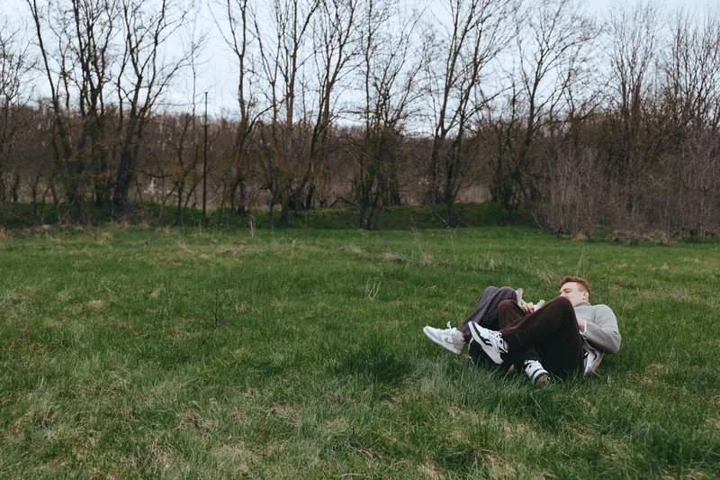 Casual person relaxing on a grassy meadow outdoors, lying on the ground with legs up, enjoying a sunny day, carefree mood, natural scenery, simple leisure moment