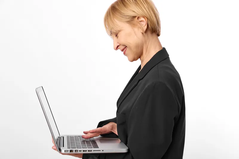 Blonde business woman in profile typing on laptop, focused expression, office work mood, using computer for communication, isolated on white background, copy space
