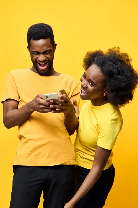 Cheerful young couple enjoying their time together with a smartphone, showcasing joy and connection against a vibrant yellow background