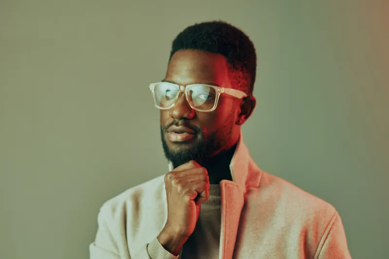 Thoughtful African man in stylish glasses posing against a colorful background, showcasing confidence and elegance in urban fashion