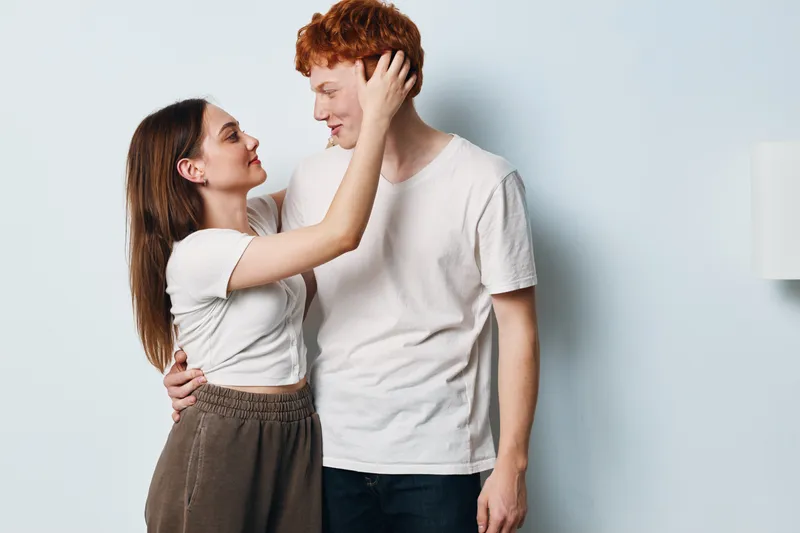 Couple, young man and woman embracing affectionately on light background. Casual clothing, smiling faces, close connection, romantic moment in indoor studio setting with soft lighting.