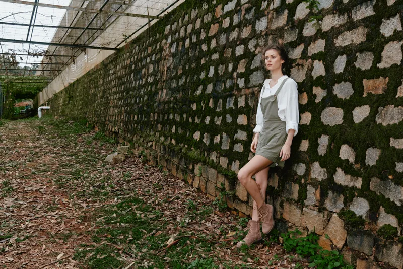 Stylish young woman in casual outfit, posing against a rustic stone wall in a green environment, evoking feelings of tranquility and connection with nature