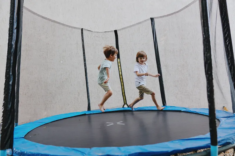 Active children playing on a trampoline, enjoying their time while jumping and laughing in a fun outdoor setting with bright colors and summer vibes.