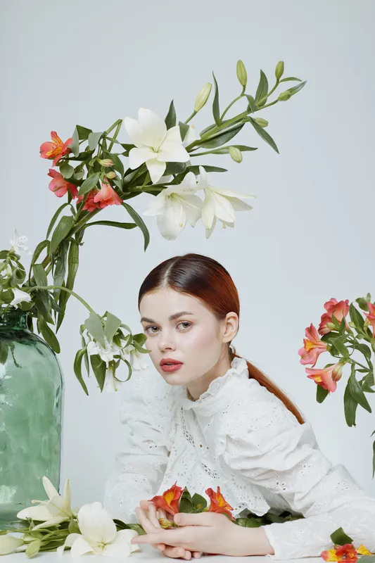 Elegant model in vintage white lace blouse surrounded by colorful flowers, showcasing beauty and serenity in a soft pastel setting