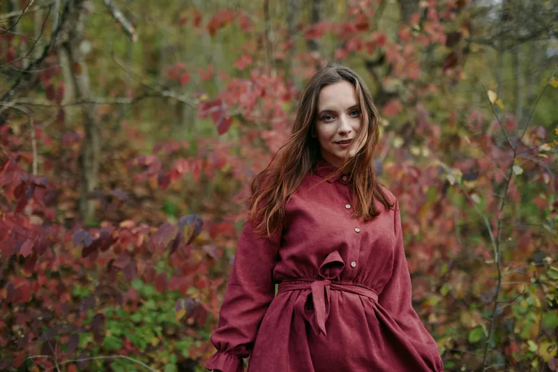 An authentic portrait captures a poised woman in a burgundy coat amid autumn foliage, using natural light and honest expression to convey credibility and relatable mood.