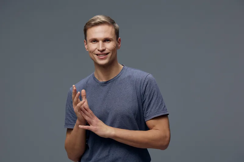 Smiling man wearing blue t-shirt looking at camera standing on grey background tech lifestyle concept