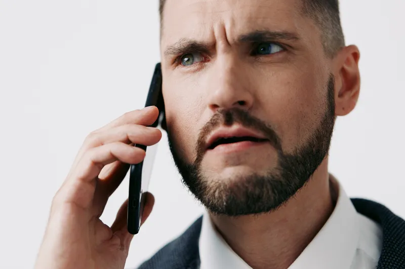 A focused business professional man on a call, displaying a tense expression, isolated colored background that emphasizes a serious mood and corporate context.
