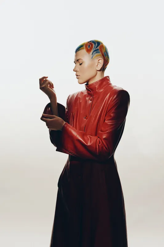 Woman with colorful short hair wearing red leather jacket, stylish pose against white background, creative fashion portrait with modern edgy style.