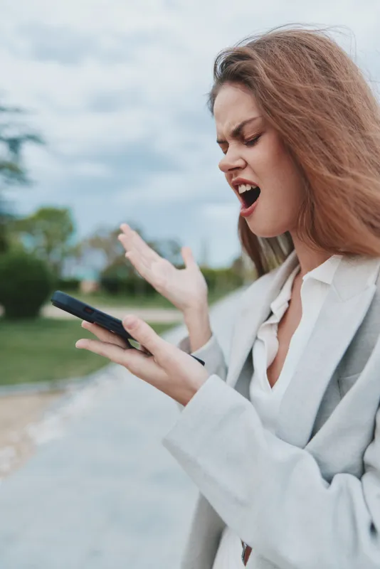 frustrated woman upset with financial crisis holding smartphone outdoors in casual business outfit