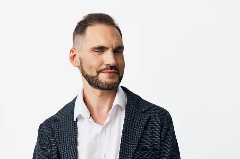 A business professional man stands against a clean white background, radiating confidence and focus. He wears a dark blazer with a white shirt, presenting a poised executive look.