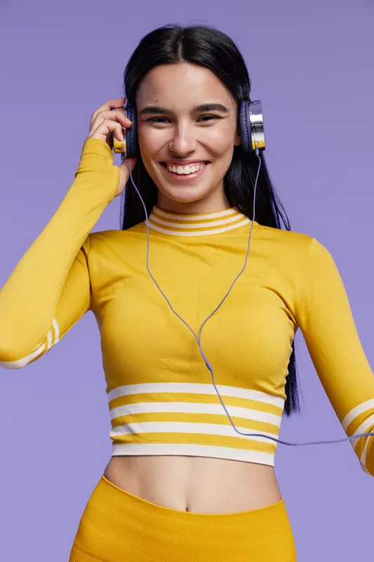 happy woman sport fitness wearing bright yellow workout clothes and headphones, smiling with a purple background, active lifestyle and positive energy.