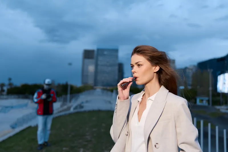 Confident woman in business attire outdoors, holding a pen, with a modern city skyline in the background, embodying professionalism and ambition.