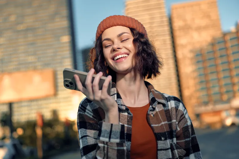 woman smile with smartphone in city street at golden hour, candid lifestyle portrait showing authenticity and emotional storytelling, mindful living vibe with warm golden glow.