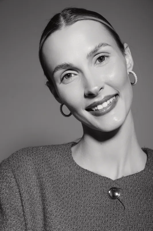 Smiling caucasian woman with pale skin and sleek hair wearing hoop earrings and textured top in studio portrait. Concept of beauty and fashion.