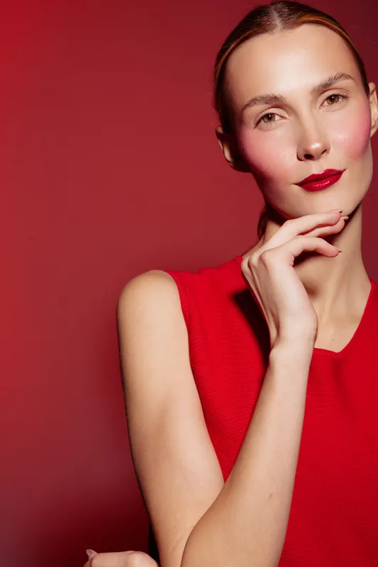 Portrait of a confident woman in red dress with red lipstick posing against red background. Concept of fashion, beauty, elegance, and style in studio lighting.