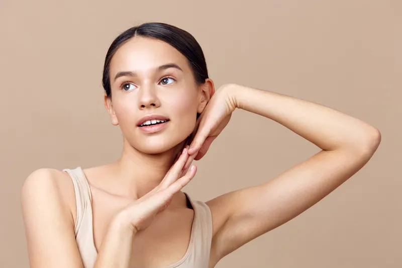 A graceful young model with soft makeup poses against a warm beige background, embodying beauty and confidence, showcasing healthy skin and a serene expression
