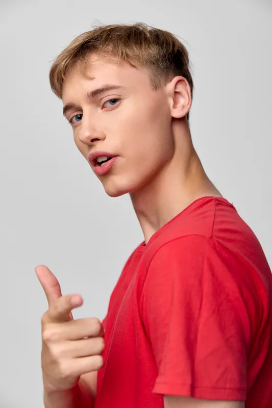 Young man in a red shirt points at the camera with confidence, conveying approachability, casual style, studio lighting, clean background, bright mood and modern fashion expression