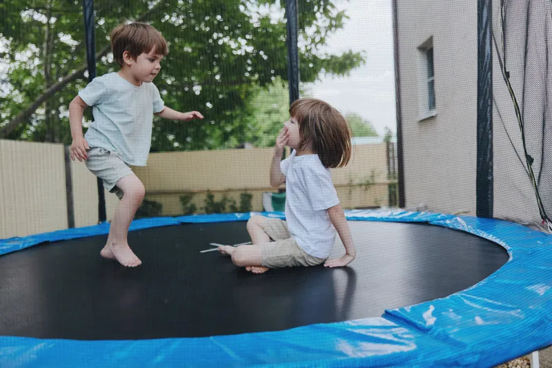 Happy children playing together on a trampoline, enjoying their time outdoors with laughter and joy under the sunny sky, showcasing carefree youth and playfulness.