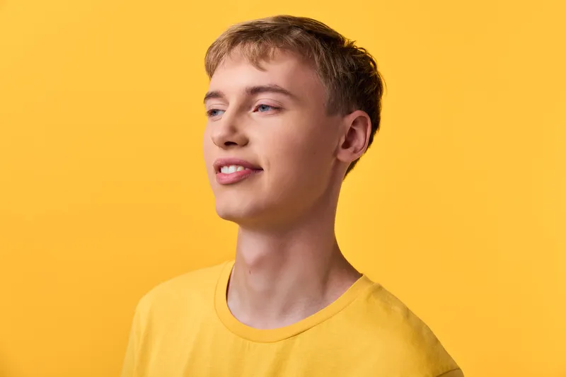 Youthful, smiling male in a yellow shirt against a bright yellow backdrop, showcasing casual style, positive mood, studio lighting, and clean composition for lifestyle and fashion projects