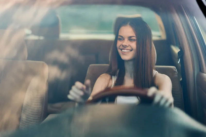 Smiling young woman driving a car, showcasing confidence and freedom while enjoying a sunny day, perfect for themes of adventure and independence.