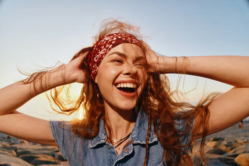 lifestyle woman with boho-western bandana and denim top laughing with joy outdoors in warm film color natural light golden hour beach background