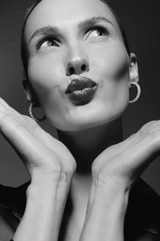 Close-up of a smiling white woman with light skin and dark hair making a playful kiss face in black and white. Concept of beauty and positive emotion.
