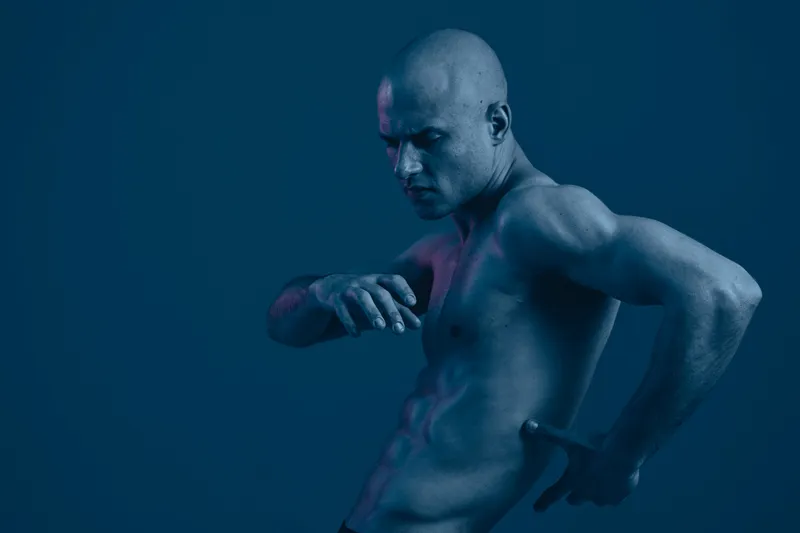 Athletic man posing in a dramatic blue lighting, showcasing strength and fitness. This black and white image captures intense emotion and artistic expression.