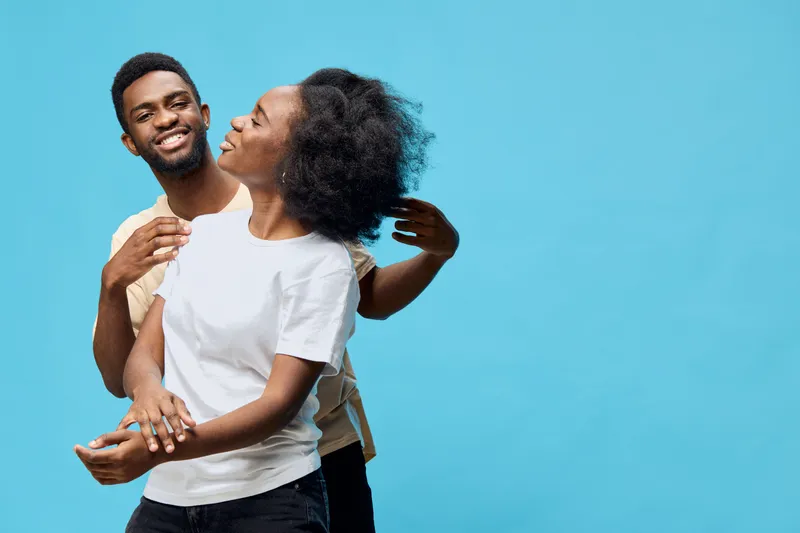Happy couple embracing with joy against a bright blue background, showcasing love, connection, and vibrant emotions in casual clothing