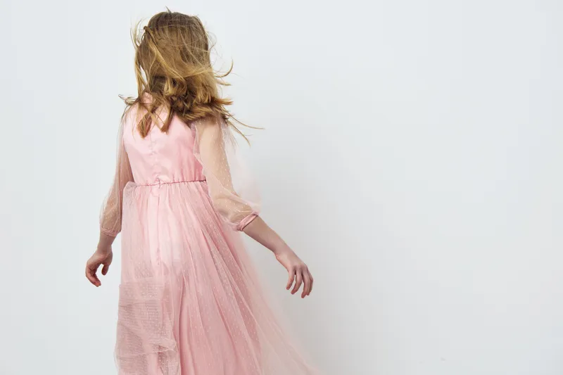 Young girl in a flowing pink dress spinning gracefully, showcasing elegance and joy in a minimalist setting with a soft color palette