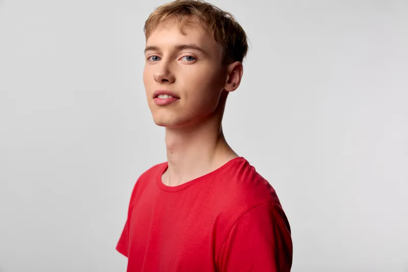 Man in a red shirt poses against a clean studio backdrop, showcasing a casual expression and confident stance for fashion, lifestyle, or model photography projects.
