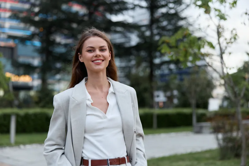 Confident woman in business attire smiling outdoors in a modern urban setting, showcasing professionalism and style for business-related concepts.