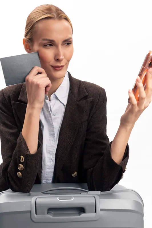 Young woman with passport and suitcase checks phone while preparing for travel. Concept of trip planning, tourism, and modern lifestyle with focus on journey and vacation.