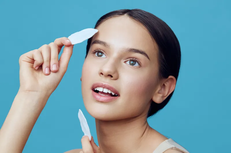 Young woman applying skincare with facial tools against a blue background, showcasing beauty and relaxation in a light and refreshing atmosphere