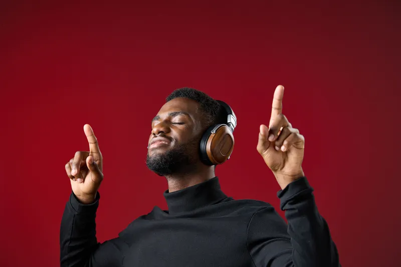 Young Black man enjoying music with headphones on a red background, expressing joy and relaxation while listening to his favorite songs