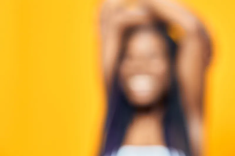 Joyful woman with long hair expressing happiness against a vibrant yellow background in a casual outfit, showcasing positivity and energy