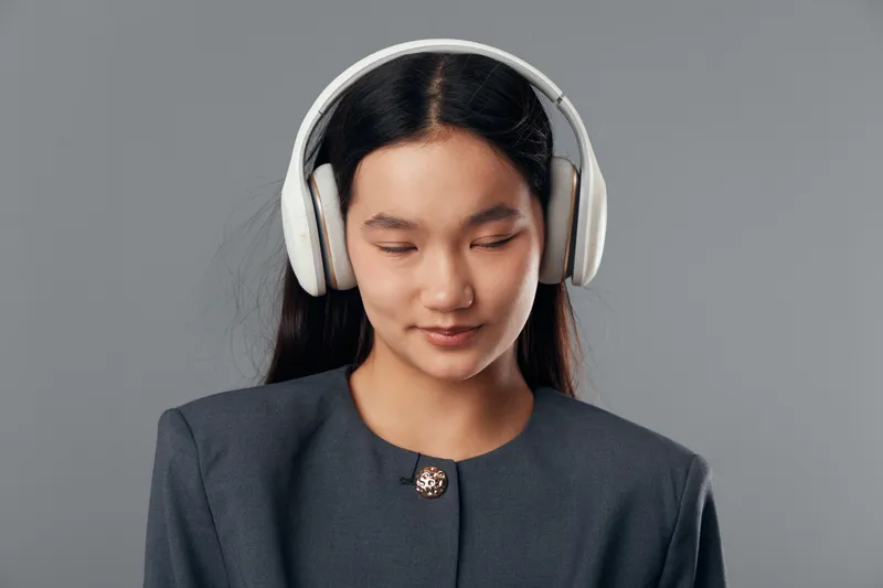 Young woman with headphones listening to music or podcast, eyes closed and relaxed. Female with long hair in smart casual outfit on gray background in studio for entertainment and audio.