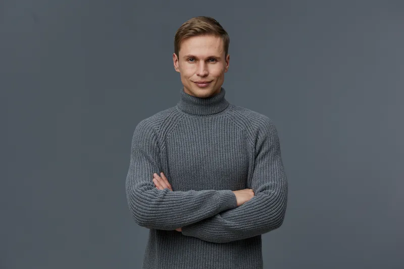 smiling man wearing gray knitted turtleneck sweater standing arms crossed looking at camera isolated on dark gray background digital nomad concept remote work communication technology
