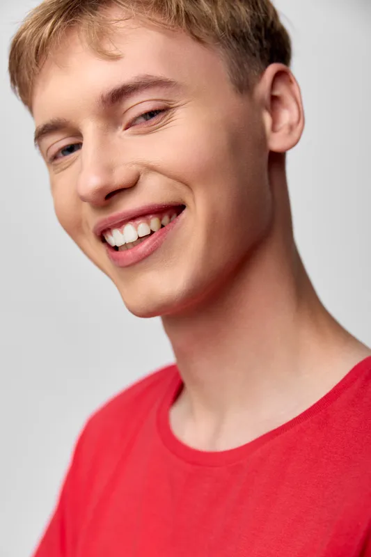 Smiling man, red shirt, close up shot highlighting a friendly expression, casual style, bright studio lighting, clean background, warm mood, approachable and confident