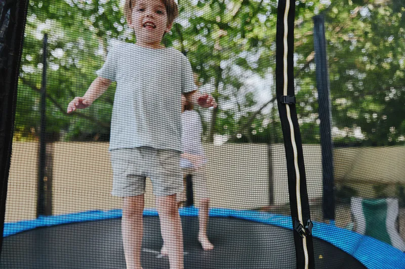 Happy children jumping on a trampoline, enjoying outdoor play in a sunny environment, surrounded by greenery and a cheerful atmosphere.